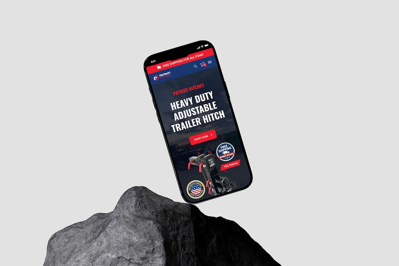 The Patriot Hitches mobile homepage on a phone balanced on a rock